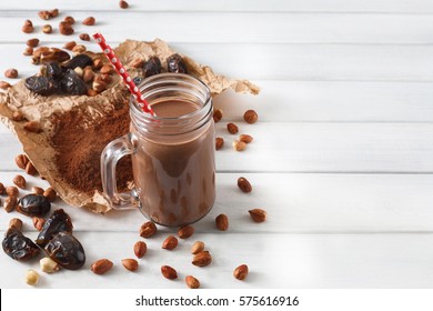 Detox cleanse drink, chocolate smoothie ingredients. Natural, organic healthy juice in glass jar for weight loss diet or fasting day. Cocoa powder, nuts, date fruit mix on white wood with copy space
