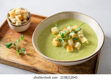 Detox cream soup of green vegetables broccoli, green peas, spinach served with crutons and micro greens on a grey concrete background. Spring detox recipe, healthy food concept. Close up