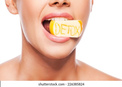 Detox diet. Close-up of beautiful young shirtless woman holding piece of apple in her mouth with detox text on it while standing against white background