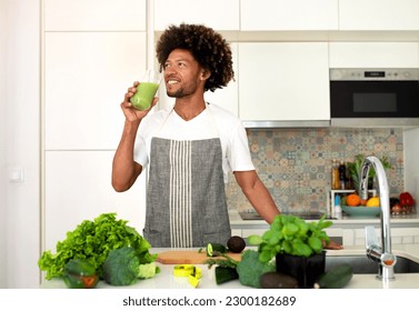 Detox Diet. Happy Black Guy Cooking And Drinking A Glass Of Green Vegetable Smoothie Standing In Modern Kitchen At Home. Healthy Weight Loss And Vegetarian Recipes Concept - Powered by Shutterstock