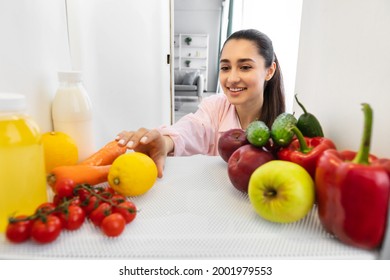 Detox And Healthy Lifestyle. Positive Arab Lady Maid Looking At Open Fridge, Taking Grabbing Lemon From The Shelf, Cooking Dish From Organic Ingredients. View From Inside The Refrigerator