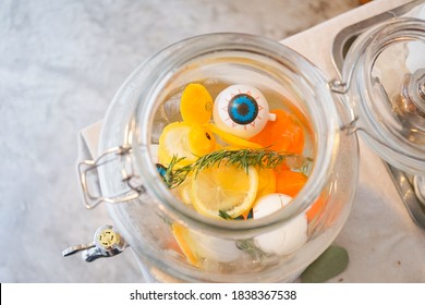 Detox infused water with fresh vegetables including mint, lemon & carrot in beverage dispenser with soft focus on the eye ball, props for Halloween. Funny idea of healthy drink served during Halloween