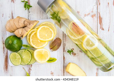 Detox Infused Water with Lemon, Lime, Ginger and Mint in Sports Bottle, with cut pieces of lemon, ginger and lime nearby