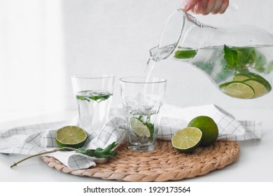 Detox water with lime fruit. Hand pouring lime fruit water from jug into glasses.