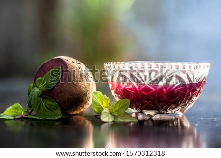 Detoxifying Beetroot extracted tincture in a glass bowl on black glossy surface with some raw fresh sliced beetroot vegetable with it used as a remedy for Inflammation in the kidney. Horizontal shot.