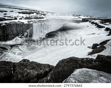 Dettifoss waterfall creating swirling patterns in icy cold water surrounded by snow and dark rocks