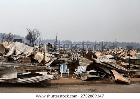 Devastated landscape following a forest fire, featuring collapsed structures, scattered debris, and abandoned chairs under a smoky sky.