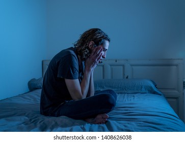 Devastated millennial man crying sad feeling hurt and hopeless suffering Depression. Depressed teenager victim of bullying or abuse sitting on bed alone in despair at night. In teenage Mental health.