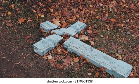 Devastated Shattered Stone Concrete Crucifix In Act Of Religious Hatred And Persecution Left On Ground Amoung Withered Autumn Foliage Leaves