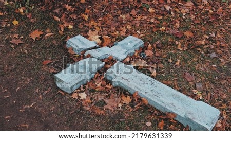 Devastated Shattered Stone Concrete Crucifix in Act of Religious Hatred and Persecution Left on Ground Amoung Withered Autumn Foliage Leaves