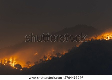 Devastating massive wildfire burning on mountain ridge at night emitting heavy smoke pollution into dark sky causing terrifying environmental disaster near Chiang Mai Thailand
