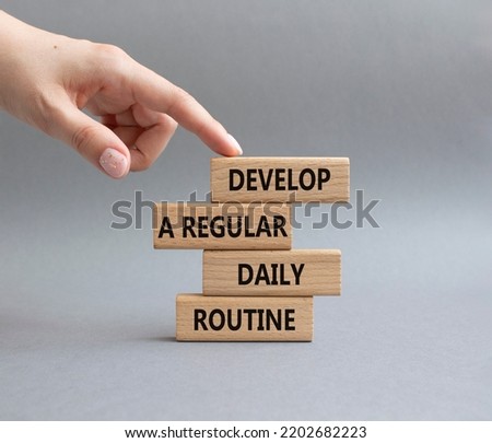 Develop a regular daily routine symbol. Concept words Develop a regular daily routine on wooden blocks. Beautiful grey background. Businessman hand. Business and concept. Copy space.