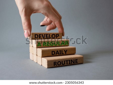 Develop a regular daily routine symbol. Concept words Develop a regular daily routine on wooden blocks. Beautiful grey background. Businessman hand. Business and concept. Copy space.