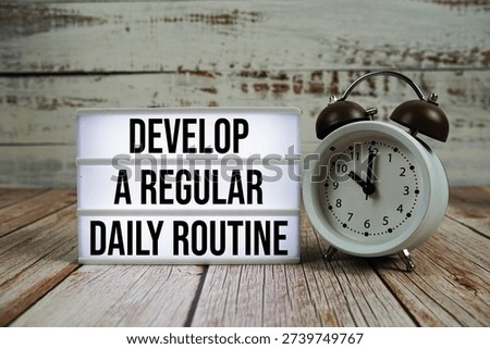 Develop a regular daily routine text on light box with alarm clock on wooden background