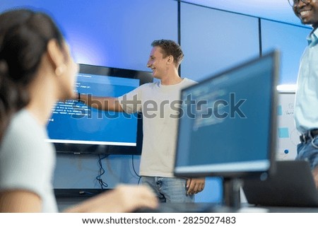 Developer points to and explains code to diverse team members, demonstrating technical knowledge transfer and inclusive group learning through collaborative code walkthrough.