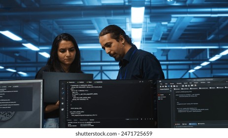 Developer in server hub using laptop to present manager plan of repairing equipment storing datasets. Specialist uses notebook to explain team leader ways of fixing rigs doing computational operations