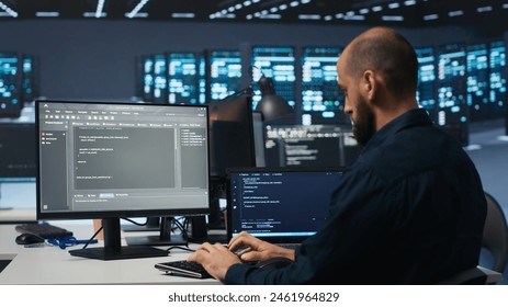 Developer typing code, working in network security data center facility, ensuring optimal performance. IT professional using desktop PC to monitor energy consumption across blade server clusters