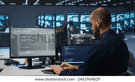 Developer typing code, working in network security data center facility, ensuring optimal performance. IT professional using desktop PC to monitor energy consumption across blade server clusters