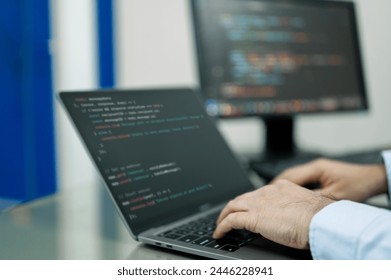Developer is typing on a laptop computer with a black screen. The laptop is open to a page with a lot of code on it. The man is focused on his work, likely programming or working on a project. Homewor