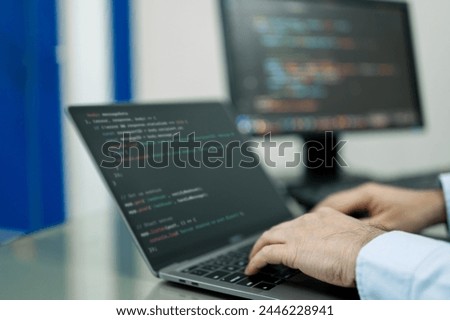 Developer is typing on a laptop computer with a black screen. The laptop is open to a page with a lot of code on it. The man is focused on his work, likely programming or working on a project. Homewor