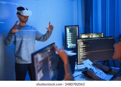 developer uses a VR headset to interact with projected interface designs, while colleagues discuss and code on screens, highlighting the integration of virtual reality and UIUX design