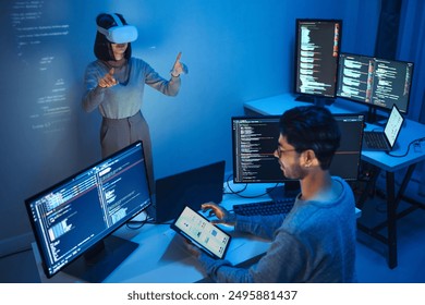 developer uses a VR headset to interact with projected interface designs, while colleagues discuss and code on screens, highlighting the integration of virtual reality and UIUX design