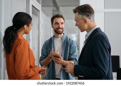 Developer using mobile phone, communication with colleagues. Multiethnic business people talking, planning start up, having meeting in modern office. Teamwork, brainstorming concept  - Shutterstock ID 1922087456