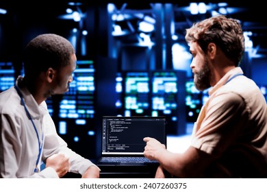 IT developers coworkers writing script code in server room on laptop terminal. Teamworking programmers doing maintenance work in technologically advanced data center updating racks software