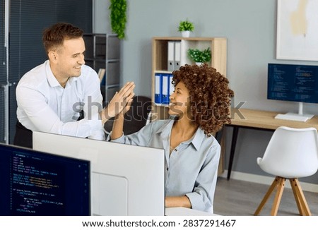 Developers programmers highfive after coding success. In a modern office, colleagues celebrate a finished feature and strong teamwork. Monitors show code. Clear concept of teamwork and success.