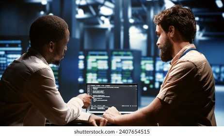IT developers team writing server script code in data center on laptop terminal. Teamworking programmers doing maintenance work in high tech facility updating rigs software