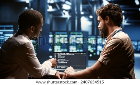 IT developers team writing server script code in data center on laptop terminal. Teamworking programmers doing maintenance work in high tech facility updating rigs software