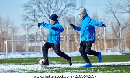 Developing ball control. Boys in blue jackets practicing dribbling on outdoor stadium with patches of snow. Precision and coordination training. Concept of sport, school, childhood, active lifestyle.