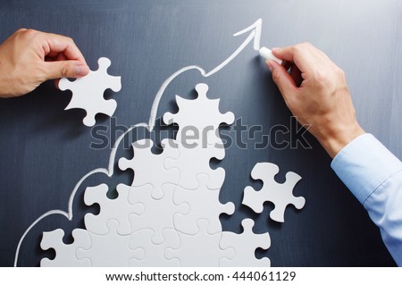 Developing growth strategy. Concept image of management and marketing. 
Working on steps shaped jigsaw puzzle. Drawing up arrow on blackboard.

