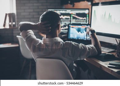 Developing New Approaches. Rear View Of Young Man In Casual Wear Holding Hand On The Back Of The Head And Working While Sitting At The Desk In Creative Office