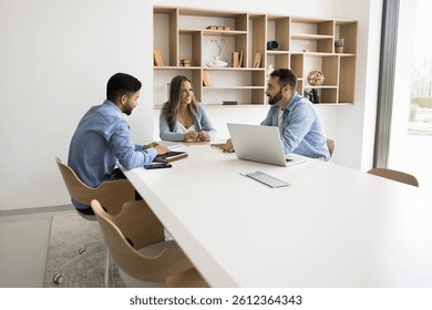 Developing new strategy. Team of three diverse multiethnic professionals gather at conference table for workshop seminar work together in business meeting to negotiate brainstorm solutions. Copy space