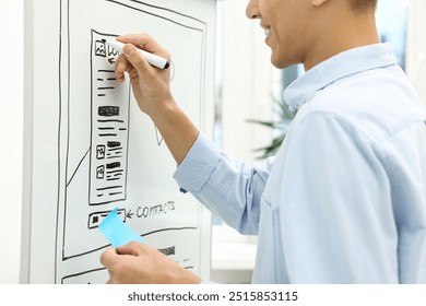 Developing UI design. Man drawing website wireframe on whiteboard indoors, closeup