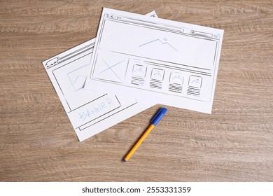 Developing UI design. Sketches of website wireframes and pen on wooden table, top view