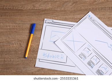 Developing UI design. Sketches of website wireframes and pen on wooden table, top view