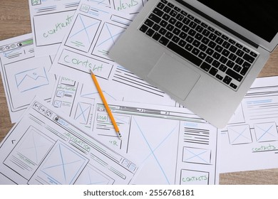 Developing UI design. Sketches of website wireframes, laptop and pencil on wooden table, top view