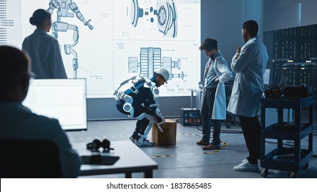 In Development Laboratory: Engineers Look At Robotics Exoskeleton Prototype Presentation With Person Testing It, Lifting Heavy Carboard Box. Designing Wearable Exosuit To Help Warehouse Workers