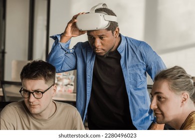 IT Development Team Working on VR Project. Man wearing VR headset, playing and touching something in the virtual world. Diverse men programmers using VR technologies and computer to create video game.