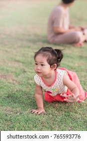 Developmental Milestones, Crawling. Cute Curly Hair Asian Baby Girl Crawling Away From Mom On The Green Grass In The Park. Baby Developmental Stages, Babyhood And Childhood Concept.