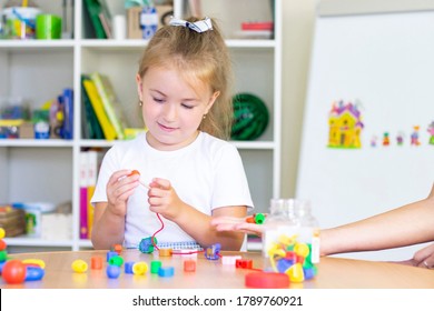 Developmental And Speech Therapy Classes With A Child Girl. Speech Therapy Exercises And Games With Beads. The Girl Has Beads In Her Hands