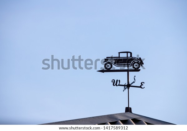 A device for displaying the wind direction with a\
figure in the form of an old retro car is installed on the roof\
against the background of a clear blue sky. Designation North,\
South, West and East.