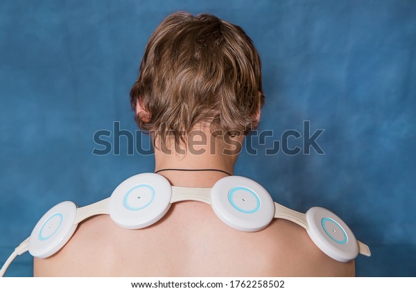 The device for magnetic therapy lies on the\
shoulders of a young man. Treatment of cervical osteochondrosis\
with a magnetic field.