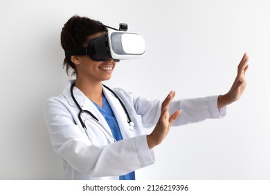 Device For Medical Education And Treatment. Happy Black Female Doctor In Coat With Stethoscope Experiencing Virtual Reality In Vr Glasses, Wearing Helmet, Isolated On White Studio Background