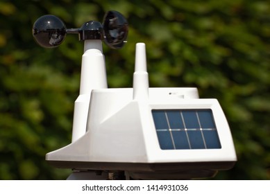 A device that measures speed, force and direction of the wind. White anemometer with solar panels on a green background.