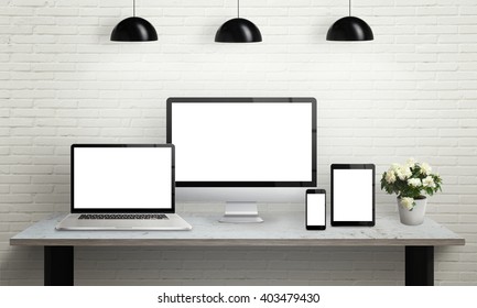 Devices On Desk With Isolated Screen For Mockup. Computer Display, Laptop, Tablet And Smart Phone On Office Desk. Flowers, Lamps And Brick Wall In Background.