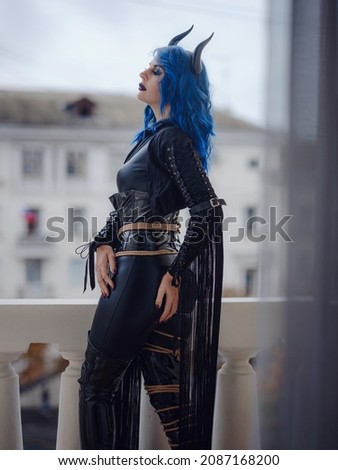 Devil. Funny imp with black horns and latex suit with shibari at Halloween party. The devil costume. woman looking at city from balcony