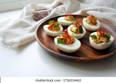 Deviled Eggs With Chinese Hot Sauce, Chilis And Scallions. Spicy Hard Boiled Egg Appetizer. Stuffed Eggs On A Wooden Plate. Light Background. Close-up. Free Space To Place Text.